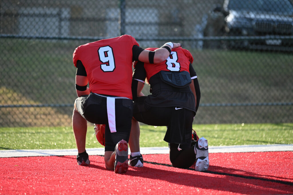 Junior Tucker Scholla (LB, #8) prays with Senior Phoenix Smith (DB, #9)