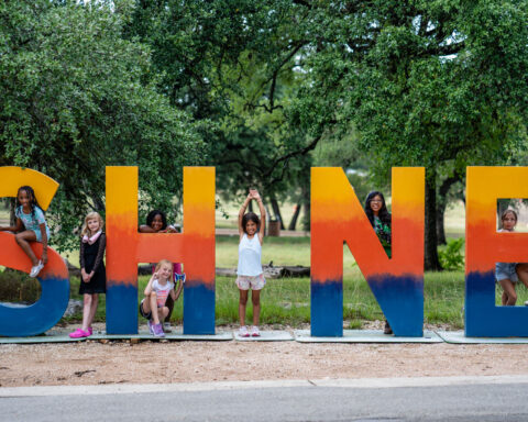 Campers pose with the “SHINE” sign at Austin Sunshine Camps