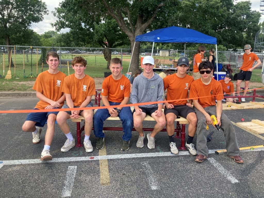 Lee Worsham and members of his work team sitting on one of the newly constructed benches at the Austin High Marching Band’s practice location