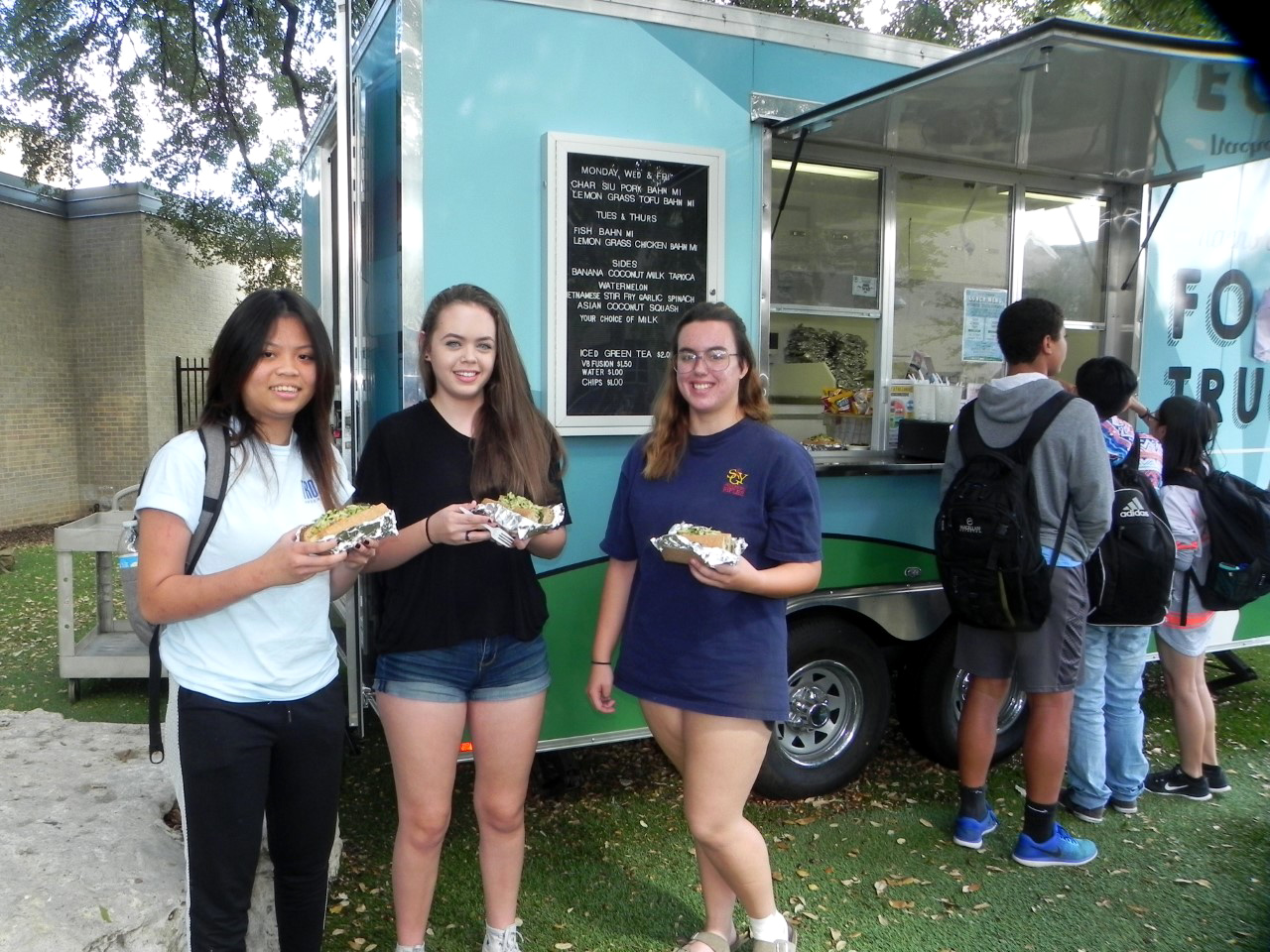 Junior Callie Quan and Sophomores Avery Ward and Elizabeth Gonzalez hold their lunch choices from the Food Truck. Callie, who is Vietnamese, states she’s usually very critical of Vietnamese food, but the food at the trailer is good. Avery is a vegetarian and the trailer staff fixes special items for her. Elizabeth, eating her first Bahn Mi and liking it, declares the food “really fresh.” Photo by Sarah Frankenfeld, Anderson HS